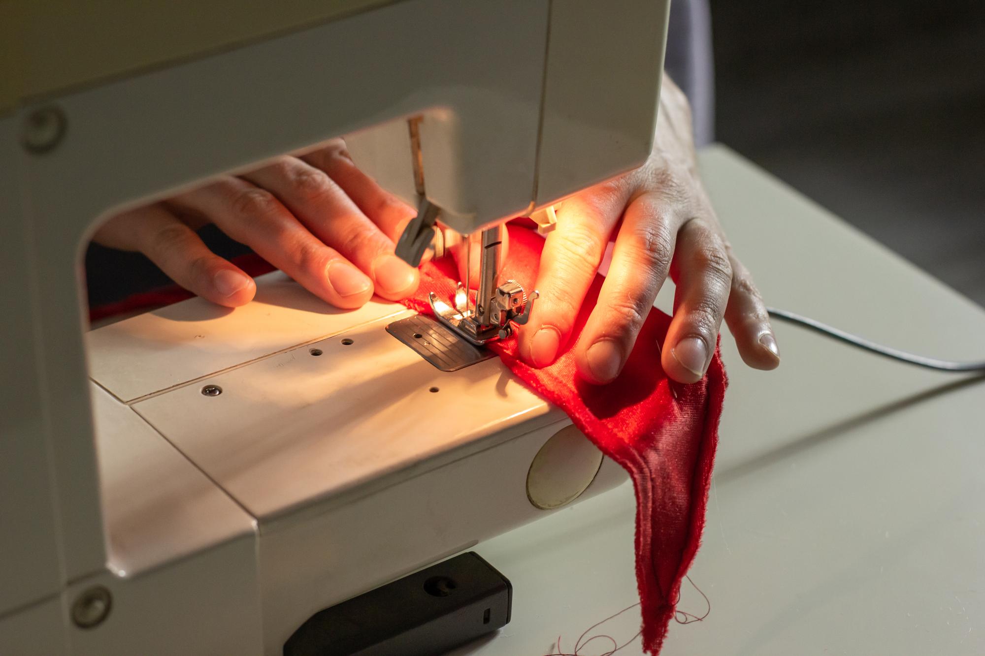 artisan hand guiding fabric under modern embroidery machine in bright studio